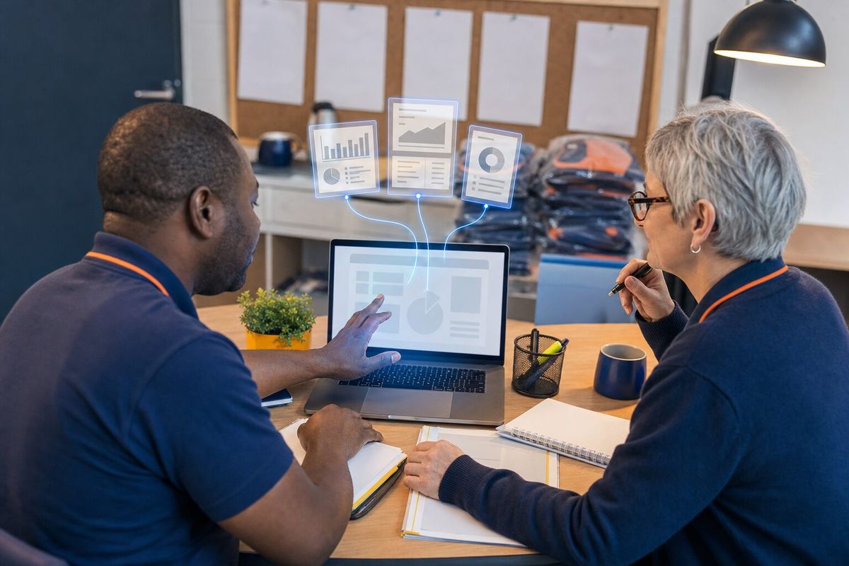 Illustrative photo: the Payroll Manager at work for the owner and office manager of a small commercial-cleaning company with hourly staff, laying out results as blue panels above a laptop.