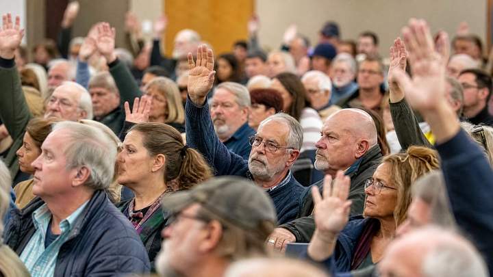 A crowded public meeting with hands raised